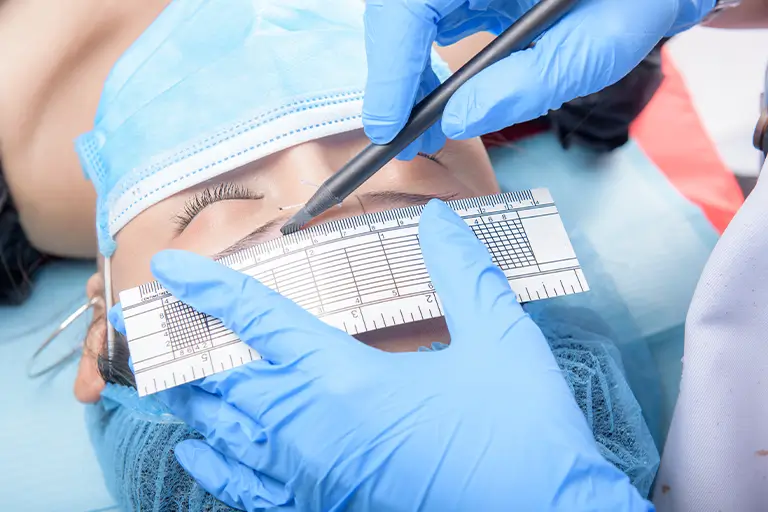 Doctor measuring and marking eyebrow shape before an eyebrow transplant procedure